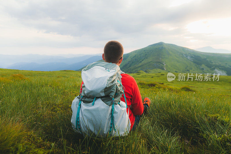 Young man backpacker relaxing at the meadow enjoying sunset in the mountains